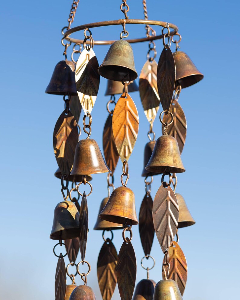 Single tiered metal wind chime with rustic copper finish featuring decorative hanging bells and leaf accents displayed in an outdoor garden setting. Handcrafted wind chimes outdoor for porch, patio, backyard, balcony, and garden decor. Metal wind chime adds soothing sounds and elegant movement to outdoor spaces. Rustic copper wind chime makes a beautiful gardener gift, gifts for mom, housewarming gift, outdoor garden decor, metal garden art, and yard decoration for every season.