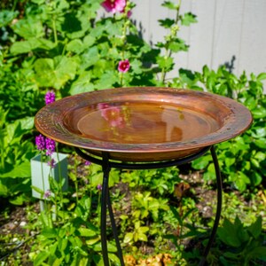 Hammered copper round birdbath with iridescent finish on curved metal stand.