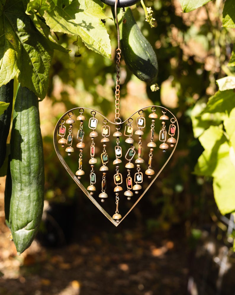 Handcrafted heart wind chime featuring colorful hanging dangles and decorative metal bells with a beautiful flamed finish. Metal wind chimes outdoor designed for garden decor, patio accents, porch decoration, balconies, fences, and backyard landscapes. Heart-shaped hanging garden ornament creates gentle, relaxing sounds while adding artistic charm to outdoor spaces. Perfect farmhouse decor, metal garden art, yard art, housewarming gift, romantic garden decor, and year-round outdoor decoration.