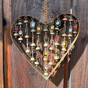 Handcrafted heart wind chime featuring colorful hanging dangles and decorative metal bells with a beautiful flamed finish. Metal wind chimes outdoor designed for garden decor, patio accents, porch decoration, balconies, fences, and backyard landscapes. Heart-shaped hanging garden ornament creates gentle, relaxing sounds while adding artistic charm to outdoor spaces. Perfect farmhouse decor, metal garden art, yard art, housewarming gift, romantic garden decor, and year-round outdoor decoration.