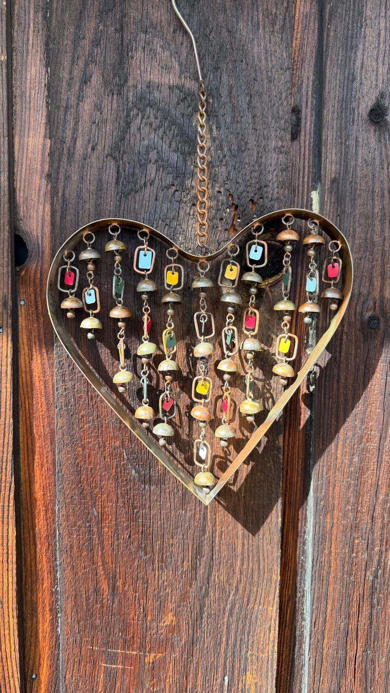 Handcrafted heart wind chime featuring colorful hanging dangles and decorative metal bells with a beautiful flamed finish. Metal wind chimes outdoor designed for garden decor, patio accents, porch decoration, balconies, fences, and backyard landscapes. Heart-shaped hanging garden ornament creates gentle, relaxing sounds while adding artistic charm to outdoor spaces. Perfect farmhouse decor, metal garden art, yard art, housewarming gift, romantic garden decor, and year-round outdoor decoration.