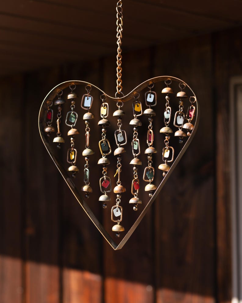 Handcrafted heart wind chime featuring colorful hanging dangles and decorative metal bells with a beautiful flamed finish. Metal wind chimes outdoor designed for garden decor, patio accents, porch decoration, balconies, fences, and backyard landscapes. Heart-shaped hanging garden ornament creates gentle, relaxing sounds while adding artistic charm to outdoor spaces. Perfect farmhouse decor, metal garden art, yard art, housewarming gift, romantic garden decor, and year-round outdoor decoration.