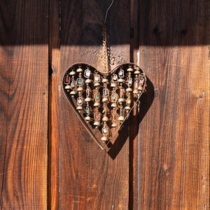 Handcrafted heart wind chime featuring colorful hanging dangles and decorative metal bells with a beautiful flamed finish. Metal wind chimes outdoor designed for garden decor, patio accents, porch decoration, balconies, fences, and backyard landscapes. Heart-shaped hanging garden ornament creates gentle, relaxing sounds while adding artistic charm to outdoor spaces. Perfect farmhouse decor, metal garden art, yard art, housewarming gift, romantic garden decor, and year-round outdoor decoration.