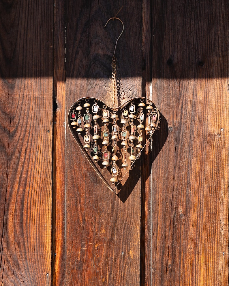 Handcrafted heart wind chime featuring colorful hanging dangles and decorative metal bells with a beautiful flamed finish. Metal wind chimes outdoor designed for garden decor, patio accents, porch decoration, balconies, fences, and backyard landscapes. Heart-shaped hanging garden ornament creates gentle, relaxing sounds while adding artistic charm to outdoor spaces. Perfect farmhouse decor, metal garden art, yard art, housewarming gift, romantic garden decor, and year-round outdoor decoration.