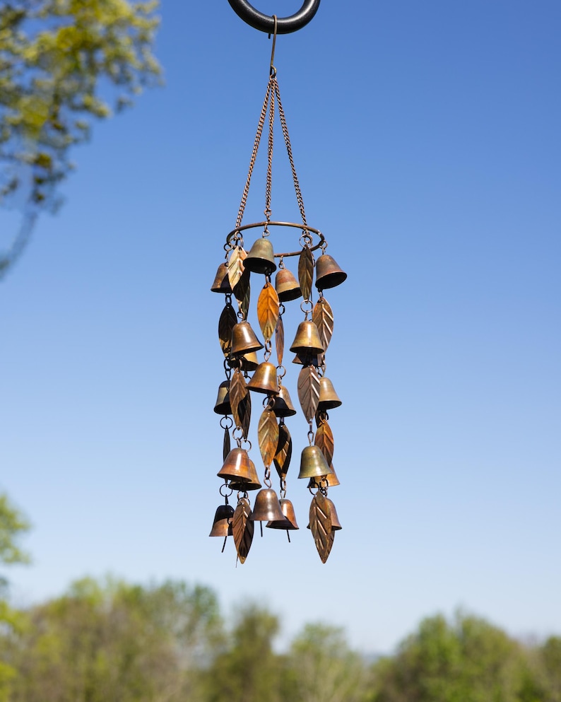 Single tiered metal wind chime with rustic copper finish featuring decorative hanging bells and leaf accents displayed in an outdoor garden setting. Handcrafted wind chimes outdoor for porch, patio, backyard, balcony, and garden decor. Metal wind chime adds soothing sounds and elegant movement to outdoor spaces. Rustic copper wind chime makes a beautiful gardener gift, gifts for mom, housewarming gift, outdoor garden decor, metal garden art, and yard decoration for every season.