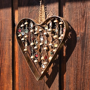Handcrafted heart wind chime featuring colorful hanging dangles and decorative metal bells with a beautiful flamed finish. Metal wind chimes outdoor designed for garden decor, patio accents, porch decoration, balconies, fences, and backyard landscapes. Heart-shaped hanging garden ornament creates gentle, relaxing sounds while adding artistic charm to outdoor spaces. Perfect farmhouse decor, metal garden art, yard art, housewarming gift, romantic garden decor, and year-round outdoor decoration.