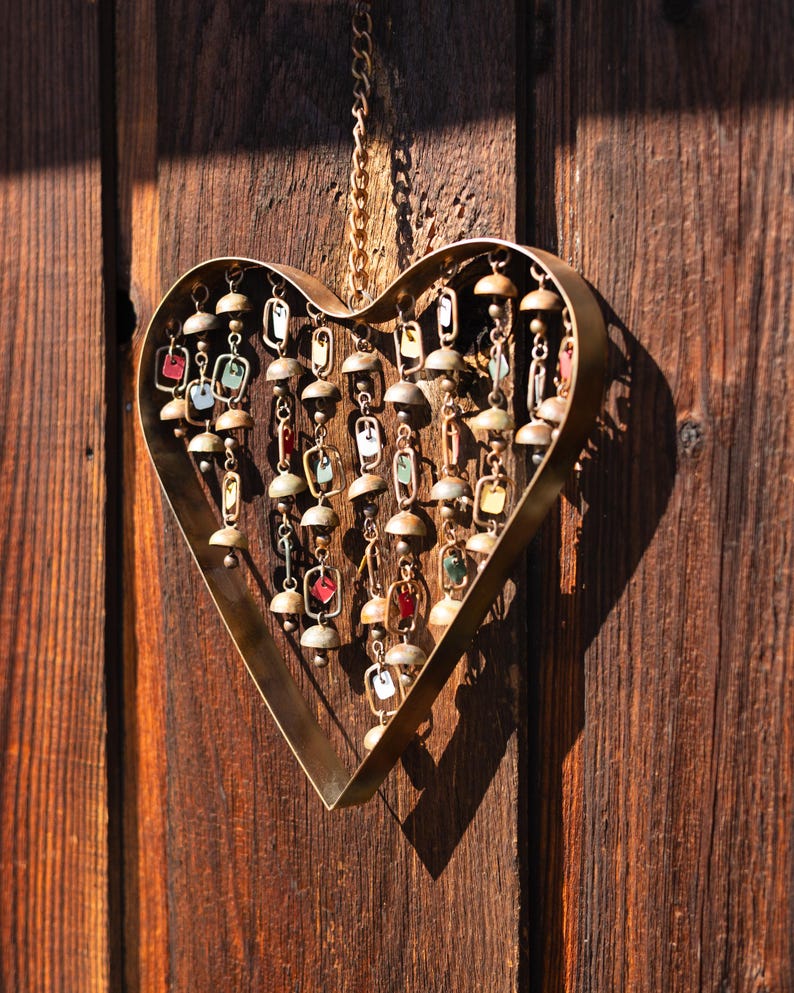 Handcrafted heart wind chime featuring colorful hanging dangles and decorative metal bells with a beautiful flamed finish. Metal wind chimes outdoor designed for garden decor, patio accents, porch decoration, balconies, fences, and backyard landscapes. Heart-shaped hanging garden ornament creates gentle, relaxing sounds while adding artistic charm to outdoor spaces. Perfect farmhouse decor, metal garden art, yard art, housewarming gift, romantic garden decor, and year-round outdoor decoration.