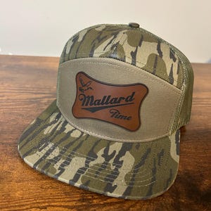 May include: A camouflage trucker hat with a brown leather patch that says "Mallard Time" and a silhouette of a duck flying.
