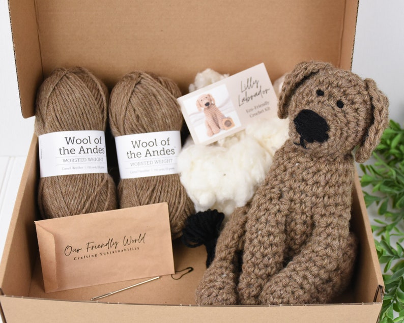 May include: A brown crochet kit for making a Labrador puppy. The kit includes two balls of brown yarn, a bag of white stuffing, a crochet hook, a needle, and a pattern. The pattern is labeled "Lilly Labrador Fine Crochet Kit".