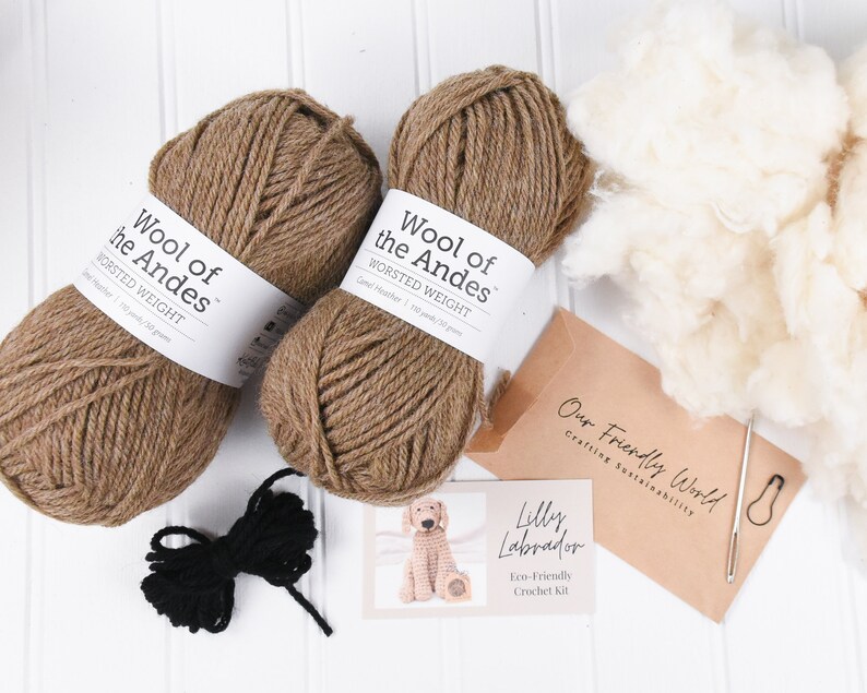 May include: A brown and black crochet kit for making a Labrador puppy. The kit includes two balls of brown yarn, a ball of black yarn, stuffing, a crochet hook, and a pattern. The yarn is labeled "Wool of the Andes" and the kit is labeled "Lilly Labrador Eco-Friendly Crochet Kit".