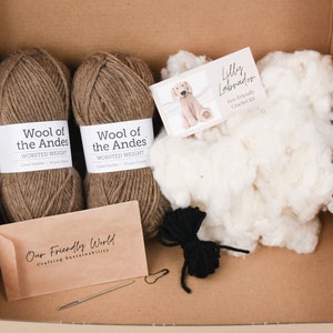 May include: A crochet kit for making a Labrador puppy. The kit includes two balls of brown yarn, stuffing, black yarn for the nose, a crochet hook, a tapestry needle, and a pattern. The yarn is labeled "Wool of the Andes Worsted Weight". The pattern is labeled "Lilly Labrador Eco-Friendly Crochet Kit".