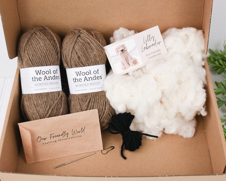 May include: A crochet kit for making a Labrador puppy. The kit includes two balls of brown yarn, stuffing, black yarn for the nose, a crochet hook, a tapestry needle, and a pattern. The yarn is labeled "Wool of the Andes Worsted Weight". The pattern is labeled "Lilly Labrador Eco-Friendly Crochet Kit".
