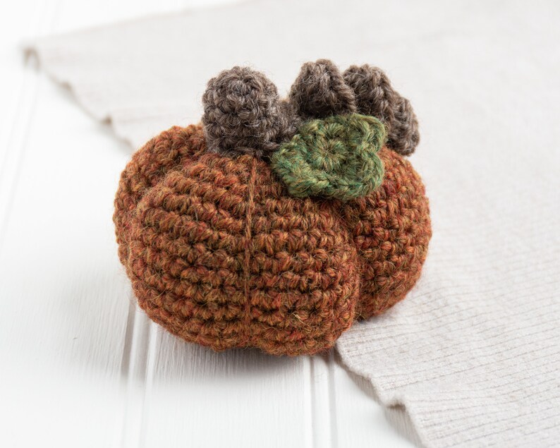 May include: A crocheted pumpkin with brown and green yarn. The pumpkin has a stem and leaves.