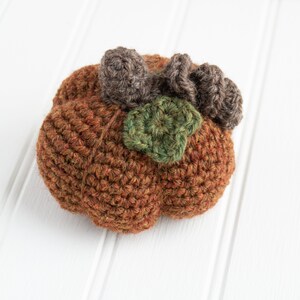 May include: A crocheted pumpkin with brown and green yarn. The pumpkin has a stem made of brown yarn and a leaf made of green yarn.