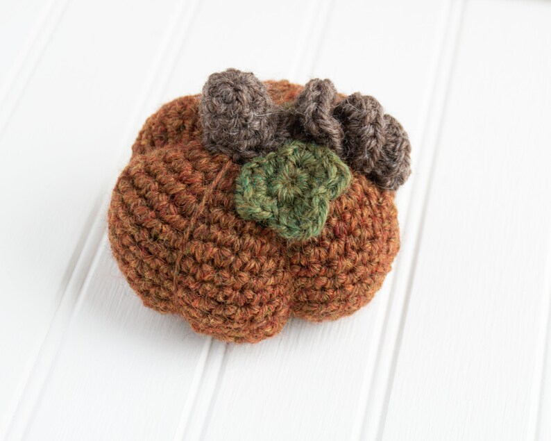 May include: A crocheted pumpkin with brown and green yarn. The pumpkin has a stem made of brown yarn and a leaf made of green yarn.