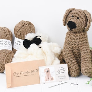 May include: A brown crochet kit for making a Labrador puppy. The kit includes brown yarn, white stuffing, black yarn for the nose and eyes, and a crochet hook. The kit also includes a card with the text "Lilly Labrador Eco-Friendly Crochet Kit" and a picture of the finished puppy.