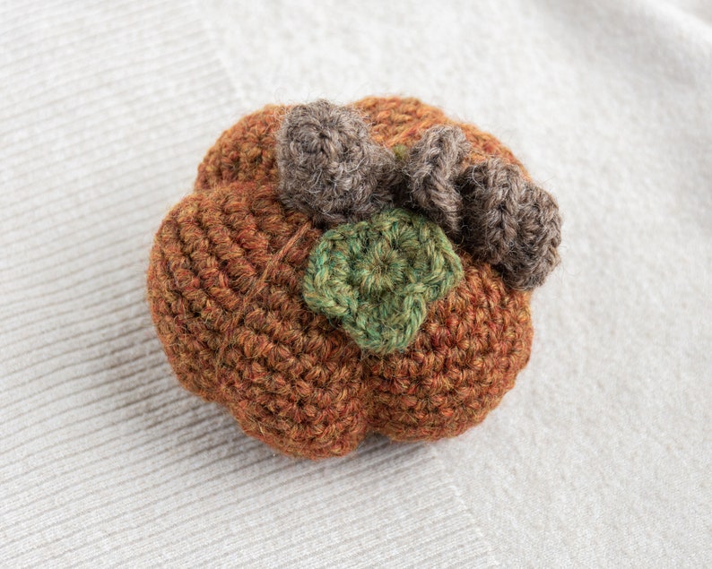 May include: A crocheted pumpkin with brown and green yarn. The pumpkin has a stem and leaves.