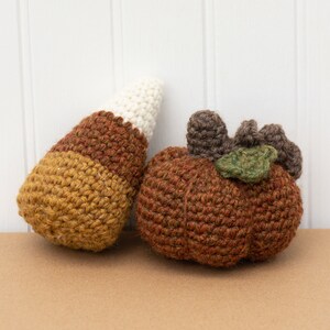 May include: Two crocheted fall decorations: a brown and white candy corn and a brown pumpkin with a green leaf.