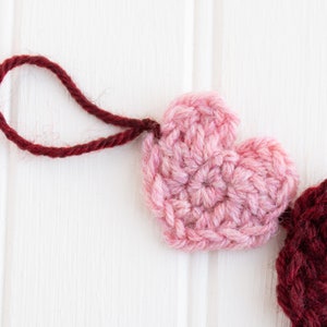 May include: A pink and burgundy crocheted heart garland with a red yarn loop for hanging.