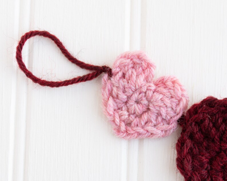 May include: A pink and burgundy crocheted heart garland with a red yarn loop for hanging.