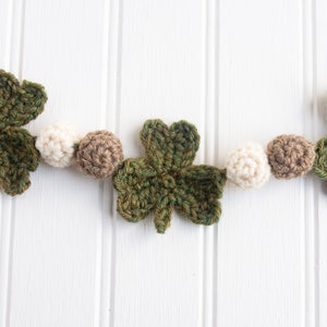 May include: A green crocheted shamrock garland with white and brown crocheted beads.
