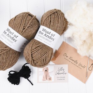 May include: A brown and black crochet kit for making a Labrador puppy. The kit includes two balls of brown yarn, a ball of black yarn, stuffing, a crochet hook, and a pattern. The yarn is labeled "Wool of the Andes" and the kit is labeled "Lilly Labrador Eco-Friendly Crochet Kit".