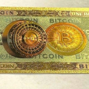 Peut inclure: Un billet Bitcoin doré avec le texte "ONE BITCOIN" et "BITCOIN" répété. Le billet présente une pièce Bitcoin et un motif circulaire détaillé. Le chiffre "1" est visible sur le billet.