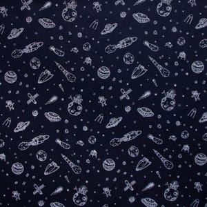 Könnte beinhalten: Ein dunkelblauer Stoff mit einem weißen, sich wiederholenden Muster aus Weltraum-Illustrationen. Das Muster enthält Planeten, Sterne, Raketen, Raumschiffe und Satelliten.