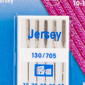 Könnte beinhalten: Eine Packung mit fünf silbernen Nähnadeln mit der Aufschrift "Jersey 130/705" und dem Prym-Logo. Die Nadeln sind in einem durchsichtigen Kunststoffgehäuse mit weißem Hintergrund verpackt. Die Verpackung ist mit "Jersey 10-14" beschriftet.