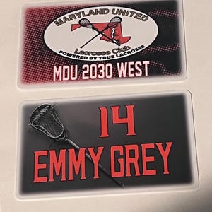 Może przedstawiać: Dwie prostokątne naklejki o tematyce lacrosse. G&oacute;rna naklejka zawiera tekst "MARYLAND UNITED" i "Lacrosse Club" z grafiką kija do lacrosse. Dolna naklejka wyświetla "14" i "EMMY GREY" z kijem do lacrosse.