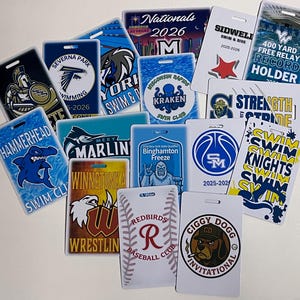 Może przedstawiać: Kolekcja prostokątnych odznak wydarzeń z r&oacute;żnymi logo drużyn i tekstem. Projekty obejmują rekina, krakena, koszyk&oacute;wkę i słowa "Swim Knights". Odznaki są w r&oacute;żnych kolorach, w tym niebieskim, białym i czerwonym.