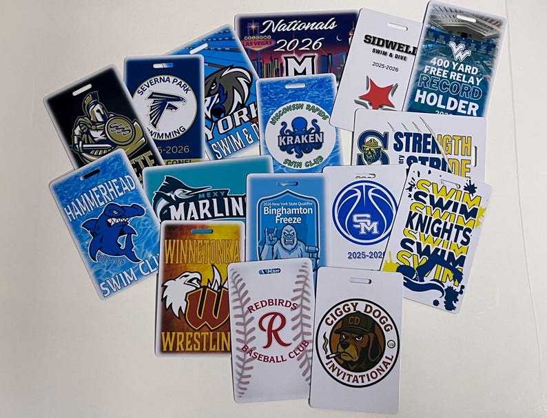 Może przedstawiać: Kolekcja prostokątnych odznak wydarzeń z r&oacute;żnymi logo drużyn i tekstem. Projekty obejmują rekina, krakena, koszyk&oacute;wkę i słowa "Swim Knights". Odznaki są w r&oacute;żnych kolorach, w tym niebieskim, białym i czerwonym.