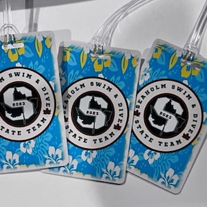 Może przedstawiać: Trzy prostokątne etykiety bagażowe z niebieskim tłem w kwiatowy wz&oacute;r. Każda etykieta ma okrągły emblemat z napisem "SEAHOLM SWIM & DIVE STATE TEAM 2023". Etykiety mają przezroczyste plastikowe pętle.