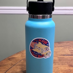 May include: A blue water bottle with a black lid and handle. The bottle has a sticker on it that says "The Magic School Bus" with a cartoon image of the bus.