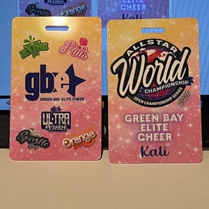 Może przedstawiać: Dwie prostokątne przepustki na wydarzenia Green Bay Elite Cheer. Jedna zawiera tekst "ALLSTAR World Championship Series 2026" i "Green Bay Elite Cheer Kali". Druga ma "gb+" i r&oacute;żne nazwy zespoł&oacute;w.