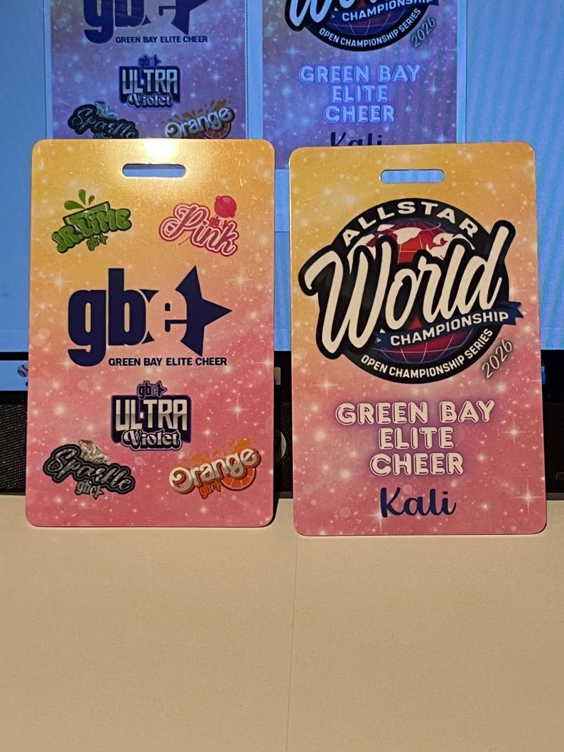 Może przedstawiać: Dwie prostokątne przepustki na wydarzenia Green Bay Elite Cheer. Jedna zawiera tekst "ALLSTAR World Championship Series 2026" i "Green Bay Elite Cheer Kali". Druga ma "gb+" i r&oacute;żne nazwy zespoł&oacute;w.
