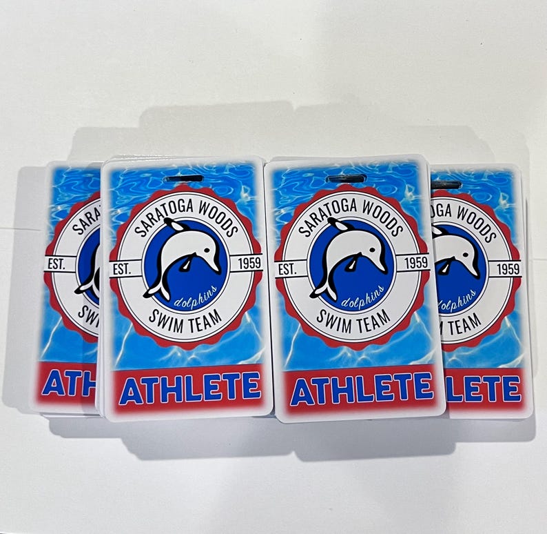 Może przedstawiać: Cztery prostokątne odznaki sportowc&oacute;w. Każda odznaka zawiera logo delfina w okrągłym emblemacie z napisem "SARATOGA WOODS SWIM TEAM" i "1959". Słowo "ATHLETE" jest wydrukowane pogrubionymi czerwonymi literami na dole każdej odznaki.