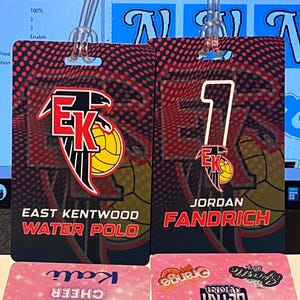 Może przedstawiać: Dwie czerwono-czarne identyfikatory drużyny piłki wodnej z napisem "EAST KENTWOOD WATER POLO" i "JORDAN FANDRICH". Identyfikatory mają czerwono-czarne tło z motywem koszyk&oacute;wki. Poniżej znajdują się dwa r&oacute;żowe identyfikatory cheerleaderek.