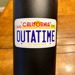 May include: Black water bottle with a white sticker that says "California Outatime The Golden State" with a yellow sun and blue text.