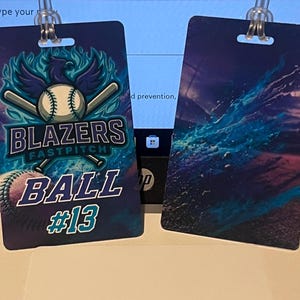 Może przedstawiać: Dwie identyfikatory z motywem baseballu. Jeden przedstawia piłkę do baseballu, kije i tekst "Blazers Fastpitch Ball #13" w kolorze niebieskim i białym na ciemnoniebieskim tle. Drugi ma niebieski i fioletowy abstrakcyjny wz&oacute;r.