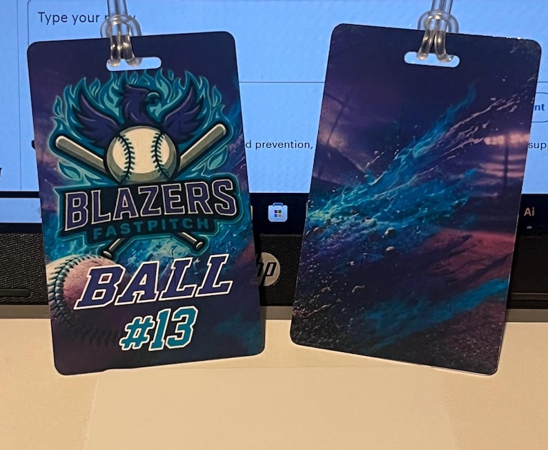 Może przedstawiać: Dwie identyfikatory z motywem baseballu. Jeden przedstawia piłkę do baseballu, kije i tekst "Blazers Fastpitch Ball #13" w kolorze niebieskim i białym na ciemnoniebieskim tle. Drugi ma niebieski i fioletowy abstrakcyjny wz&oacute;r.