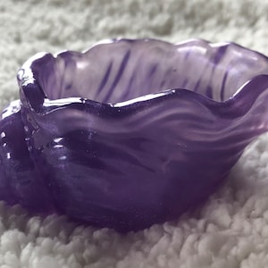 Può includere: Un piatto a forma di conchiglia viola con una finitura lucida. La conchiglia ha un motivo a spirale ed è fatta di vetro.