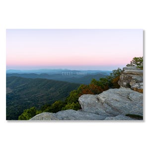 May include: A panoramic view of a mountain range with a rocky cliff in the foreground. The sky is a soft pink and purple, and the mountains are covered in green trees. The text "COAST - SUMMIT" is visible in the middle of the image.