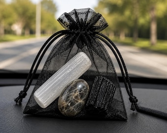 May include: A black sheer organza drawstring pouch containing three stones: a long, white, vertically striated selenite wand, a smooth, oval-shaped, dark gray and brown mottled stone, and a short, black, vertically grooved tourmaline crystal.