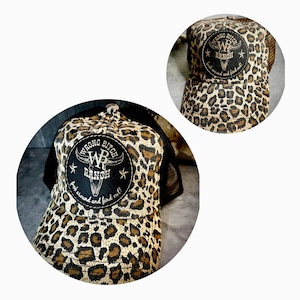 Op de afbeelding: Een zwarte en bruine truckercap met luipaardprint en een zwart leren patch met de tekst "Wrong Bitch Ranch" met een schedel- en kruisbeenderenontwerp. De tekst op de patch luidt "boot around and find out!"