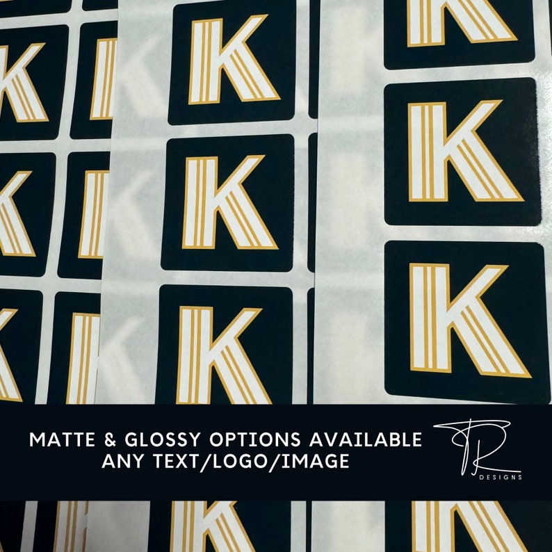 May include: A sheet of stickers with a gold letter K on a black background. The text "Matte & Glossy Options Available Any Text/Logo/Image" is at the bottom of the image.