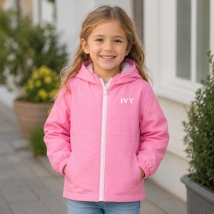 May include: A bright pink hooded jacket with a white front zip and the name IVY printed in white on the upper left chest. The jacket features long sleeves with elasticated cuffs and two front pockets, providing a simple and functional design.