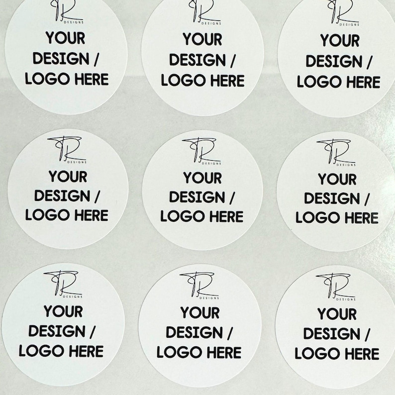 May include: A sheet of nine circular white stickers arranged in a grid. Each sticker features a black line-art logo at the top with the text TR DESIGNS, followed by the bold black text YOUR DESIGN / LOGO HERE centered on the white background.