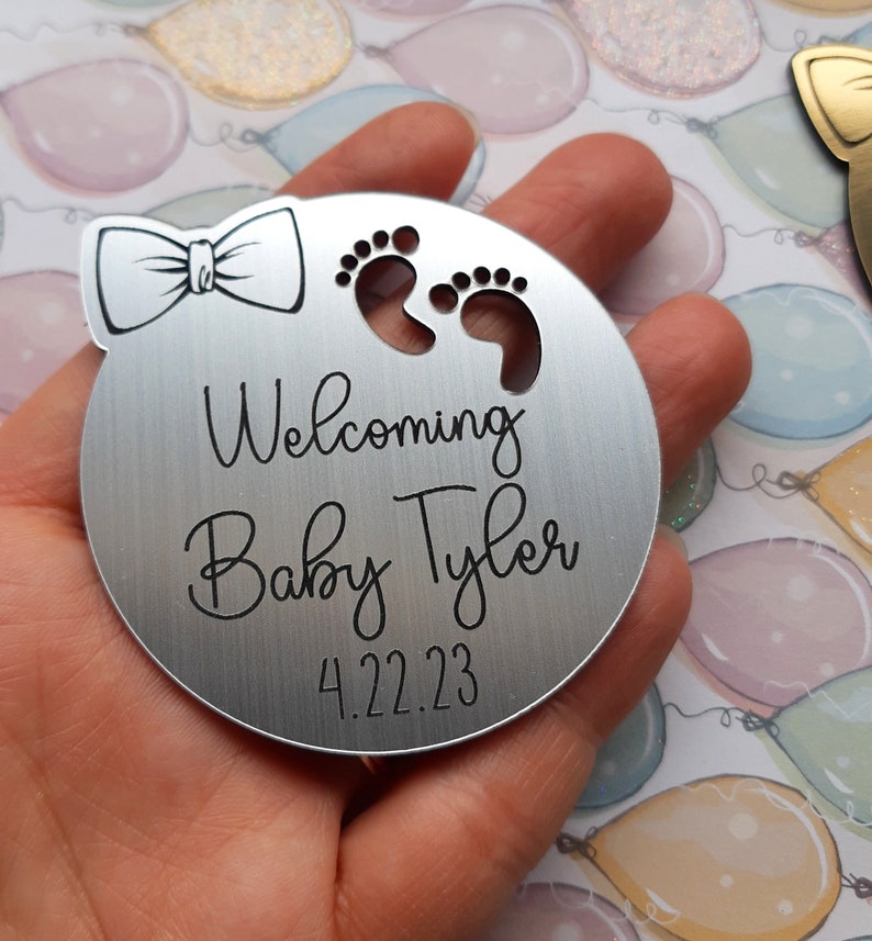 Op de afbeelding: Zilveren rond ornament met een strik, voetafdrukken en de tekst "Welkom Baby Tyler 4.22.23".