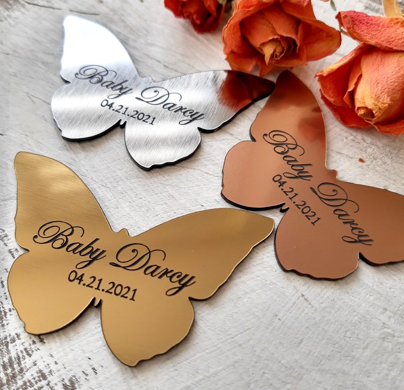 May include: Three butterfly-shaped metal ornaments with the text "Baby Darcy" and the date "04.21.2021" engraved on each. The butterflies are silver, gold, and copper.